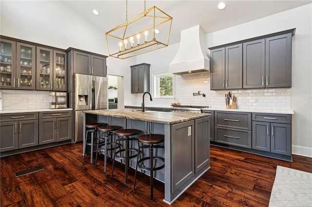 kitchen with a sink, glass insert cabinets, custom range hood, appliances with stainless steel finishes, and dark wood-style flooring