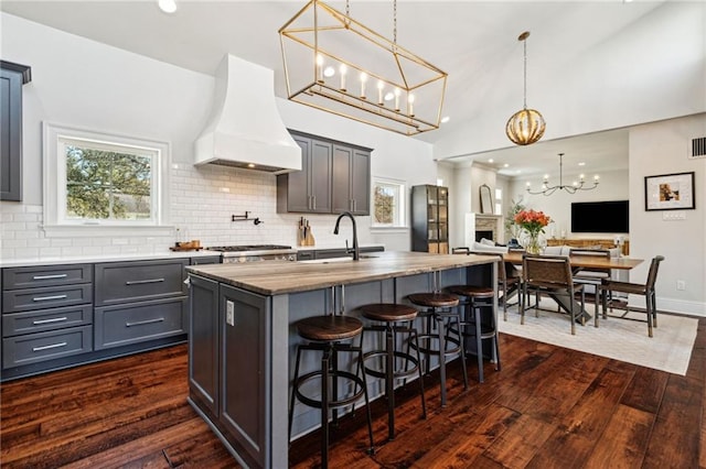 kitchen featuring dark wood finished floors, an island with sink, custom range hood, a kitchen breakfast bar, and a sink