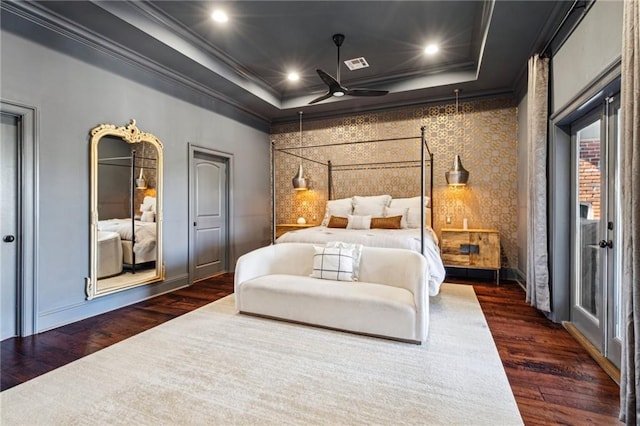 bedroom with a tray ceiling, visible vents, dark wood-type flooring, and ornamental molding