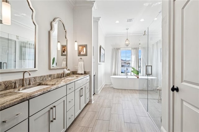 full bath featuring a freestanding bath, crown molding, visible vents, and a sink