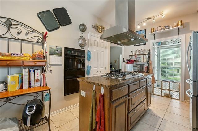 kitchen with island exhaust hood, a center island, dark stone counters, appliances with stainless steel finishes, and light tile patterned floors