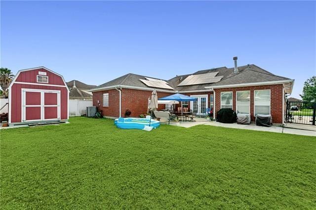 rear view of house with solar panels, french doors, a fenced backyard, an outbuilding, and a storage unit