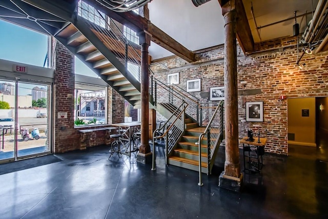 stairway with beamed ceiling, brick wall, and a towering ceiling