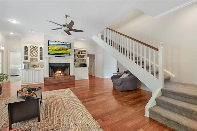 living area featuring light wood-type flooring, a warm lit fireplace, ornamental molding, and stairway