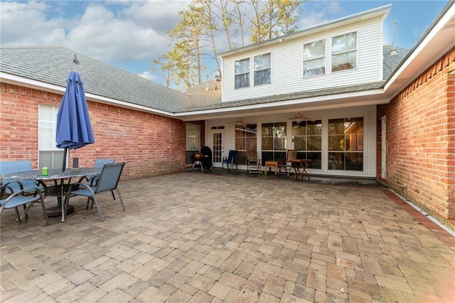 rear view of house with roof with shingles, outdoor dining area, brick siding, ceiling fan, and a patio area