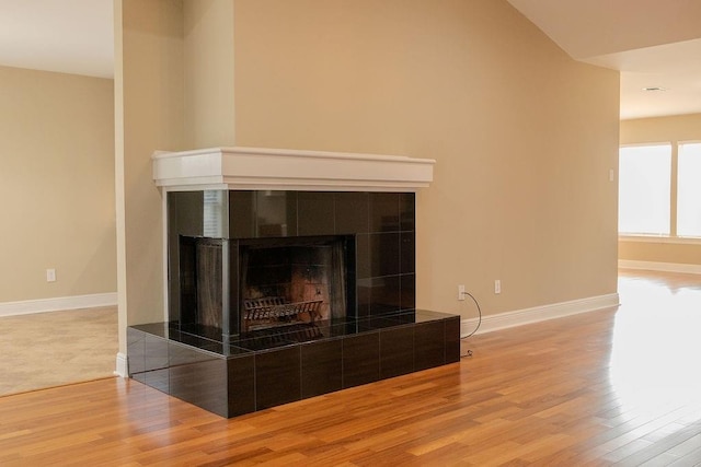 interior details with a tiled fireplace, wood finished floors, and baseboards