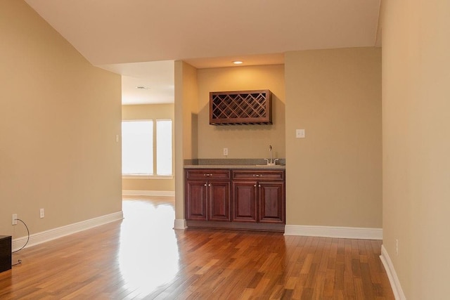 interior space with a sink, indoor wet bar, baseboards, and light wood-style floors