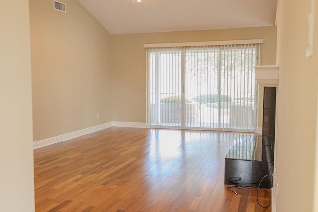 unfurnished room with vaulted ceiling, wood finished floors, visible vents, and baseboards