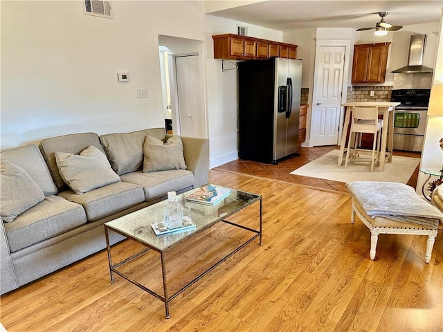 living area with visible vents, baseboards, light wood-style flooring, and a ceiling fan