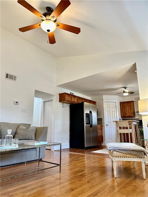 living area featuring light wood-type flooring, visible vents, lofted ceiling, and baseboards