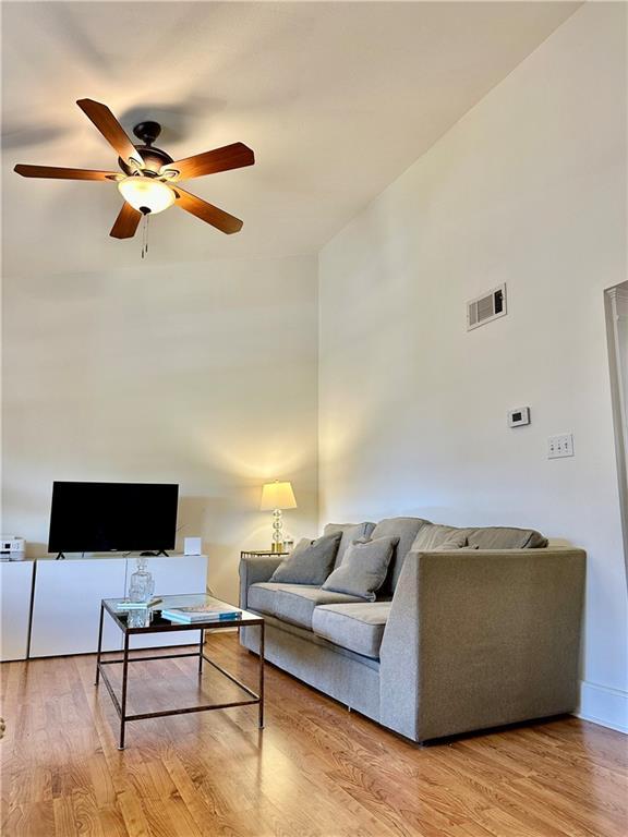 living room with a towering ceiling, visible vents, wood finished floors, and a ceiling fan