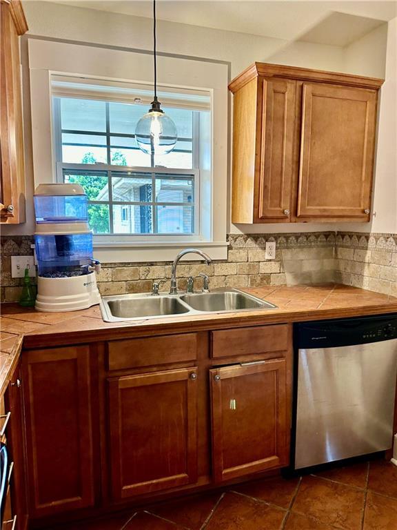 kitchen featuring a sink, brown cabinets, backsplash, and dishwasher