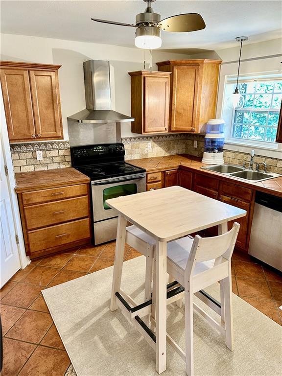 kitchen with a sink, appliances with stainless steel finishes, wall chimney range hood, brown cabinets, and backsplash