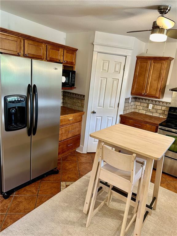 kitchen featuring dark tile patterned floors, tasteful backsplash, electric range oven, stainless steel fridge, and brown cabinetry