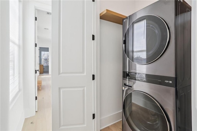 laundry room with laundry area, baseboards, stacked washer / drying machine, and light wood finished floors