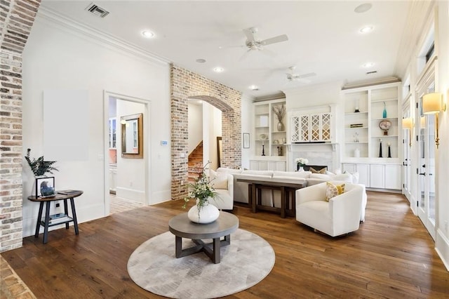 living area with dark wood-style floors, visible vents, a fireplace, arched walkways, and crown molding