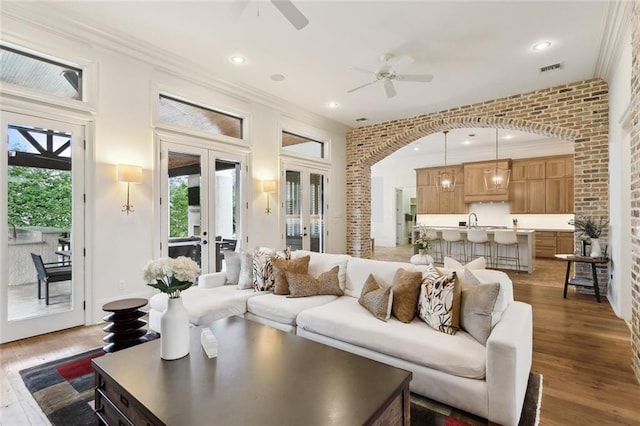 living room featuring french doors, brick wall, light wood-type flooring, and ornamental molding