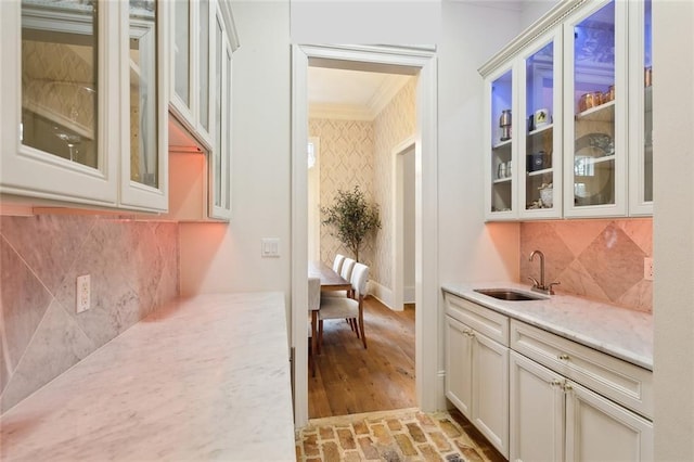 bar with a sink, backsplash, crown molding, wallpapered walls, and brick floor