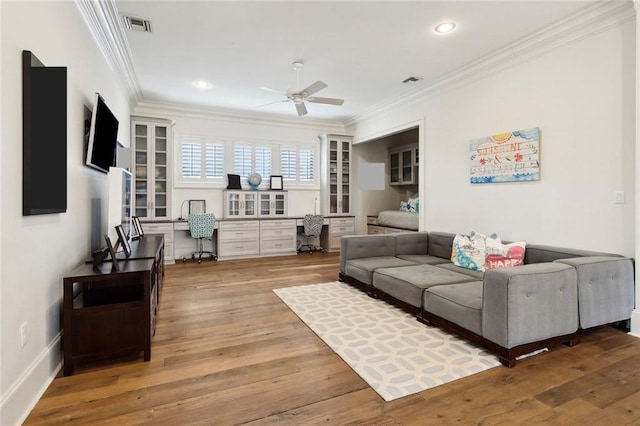 living room with visible vents, a ceiling fan, wood finished floors, built in desk, and crown molding