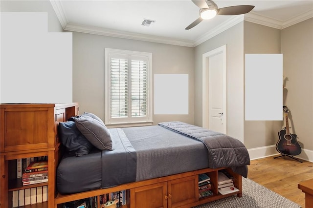 bedroom with visible vents, light wood-style flooring, crown molding, baseboards, and ceiling fan