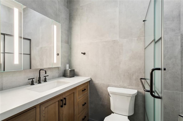 bathroom featuring a shower with door, toilet, vanity, and tile walls