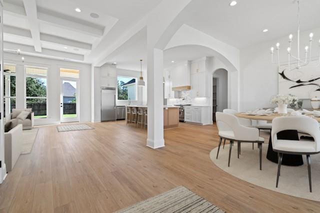 dining room with coffered ceiling, light wood finished floors, an inviting chandelier, arched walkways, and beamed ceiling