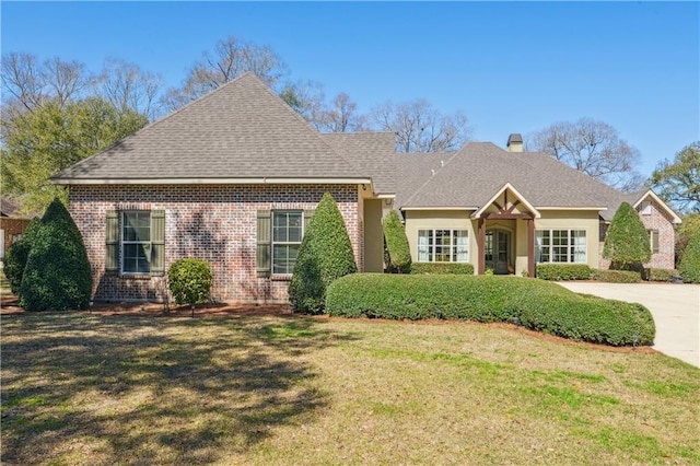 view of front of property featuring brick siding, a chimney, a front lawn, and roof with shingles