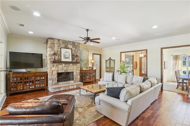 living area with visible vents, a stone fireplace, dark wood-style floors, and ornamental molding