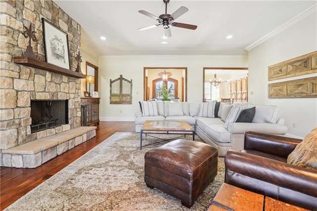 living room with crown molding, baseboards, ceiling fan with notable chandelier, a fireplace, and wood finished floors