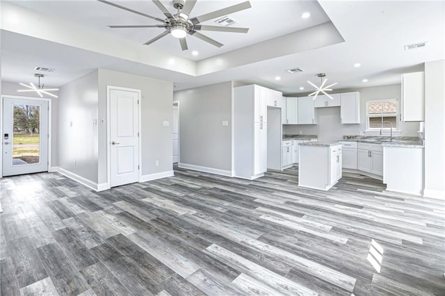 kitchen with a kitchen island, baseboards, ceiling fan, open floor plan, and a raised ceiling