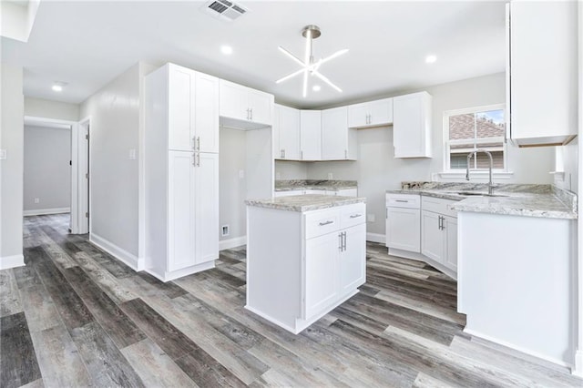 kitchen with wood finished floors, light stone countertops, visible vents, a sink, and white cabinetry