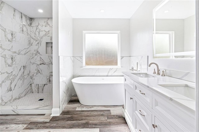 full bathroom featuring a freestanding tub, a sink, wood finished floors, a marble finish shower, and double vanity