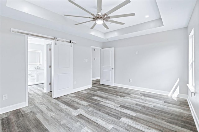 unfurnished bedroom featuring a raised ceiling, a barn door, wood finished floors, and baseboards