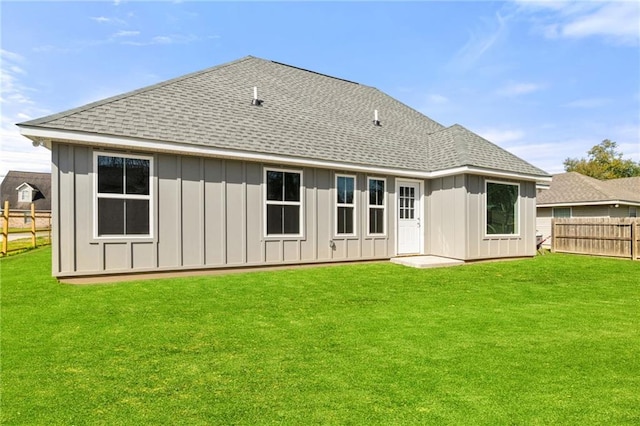 back of property featuring a yard, roof with shingles, board and batten siding, and fence