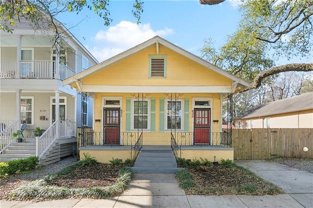 shotgun-style home featuring covered porch and fence