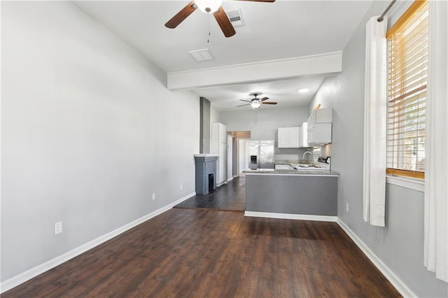 unfurnished living room featuring a ceiling fan, baseboards, dark wood-type flooring, and a sink