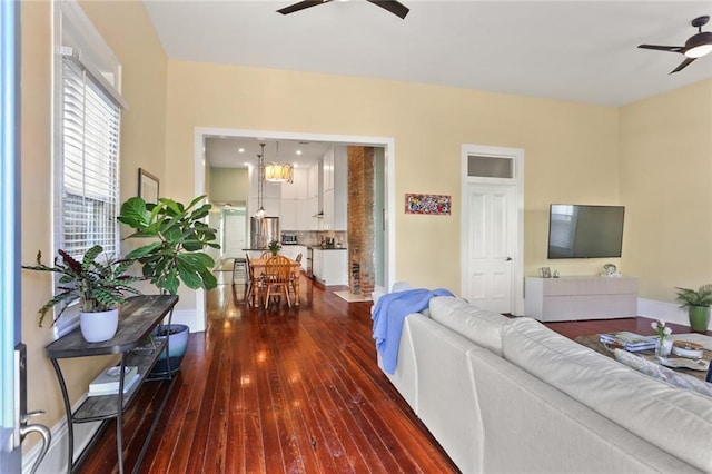 living room with ceiling fan with notable chandelier, dark wood-style flooring, and baseboards