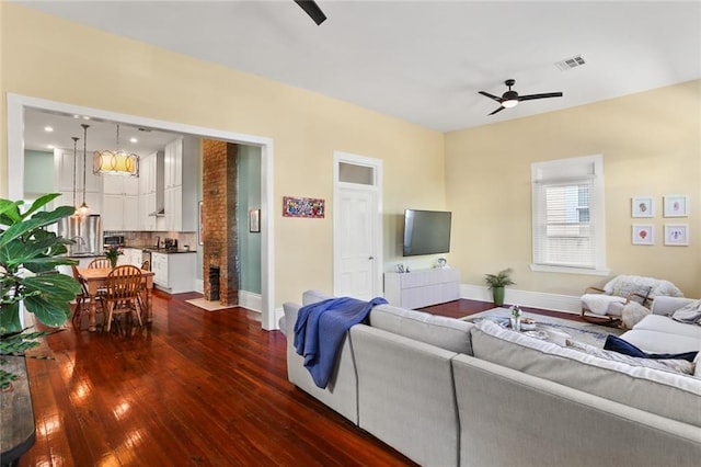 living room featuring visible vents, baseboards, dark wood-type flooring, and a ceiling fan