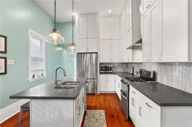 kitchen with dark wood-style floors, a sink, stainless steel appliances, dark countertops, and backsplash