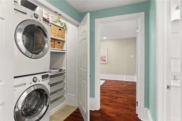 clothes washing area featuring laundry area, wood finished floors, baseboards, and stacked washing maching and dryer