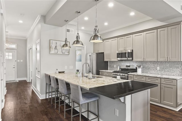 kitchen featuring visible vents, gray cabinets, appliances with stainless steel finishes, crown molding, and a kitchen breakfast bar