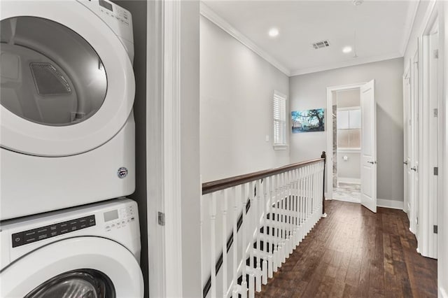 clothes washing area featuring visible vents, ornamental molding, stacked washing maching and dryer, wood-type flooring, and baseboards