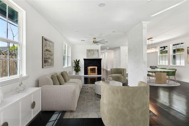 living room featuring crown molding, a brick fireplace, wood finished floors, and a healthy amount of sunlight