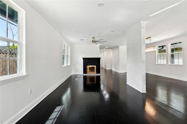 unfurnished living room featuring a healthy amount of sunlight, a brick fireplace, ceiling fan, decorative columns, and dark wood-style flooring