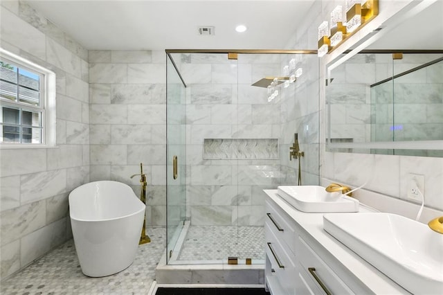 bathroom featuring a sink, tile walls, a shower stall, double vanity, and a soaking tub