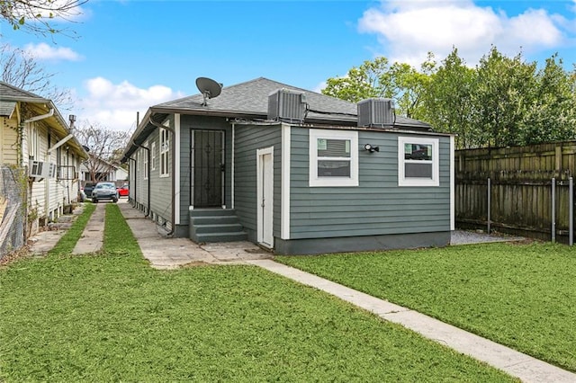 back of property featuring fence, roof with shingles, entry steps, central air condition unit, and a lawn