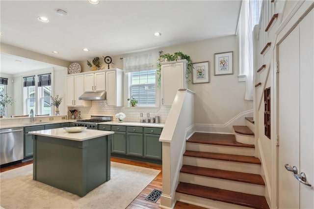 kitchen featuring green cabinets, a sink, under cabinet range hood, dishwasher, and range