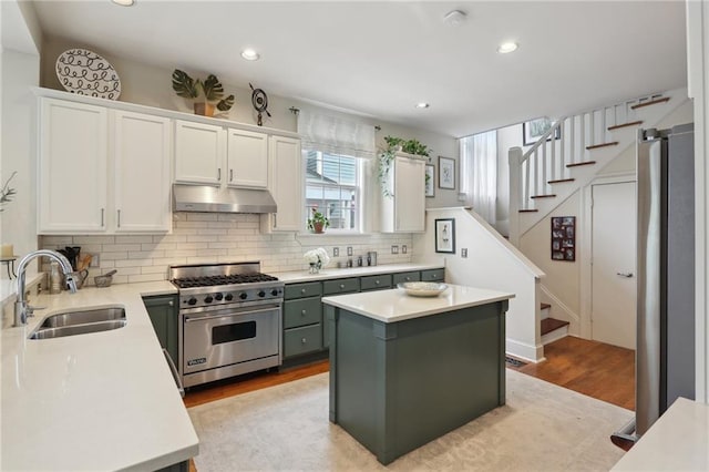 kitchen featuring a sink, under cabinet range hood, designer stove, white cabinets, and light countertops