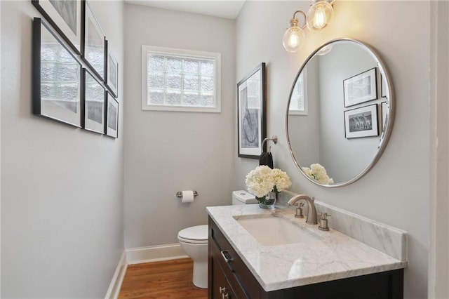 half bathroom with baseboards, toilet, wood finished floors, and vanity