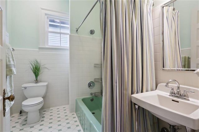 full bath featuring toilet, shower / tub combo with curtain, wainscoting, tile walls, and a sink